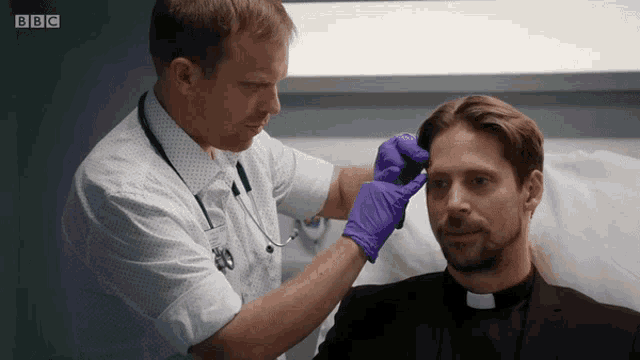 a man in a priest 's robe is being examined by a doctor with a bbc logo in the background