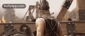 a man in a knight 's helmet is standing in front of a wooden structure .