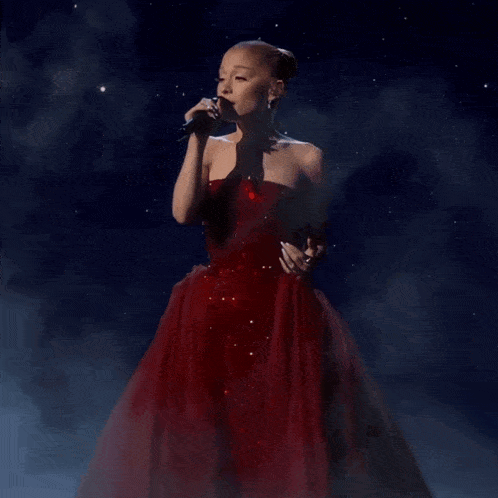 a woman singing into a microphone in a red dress