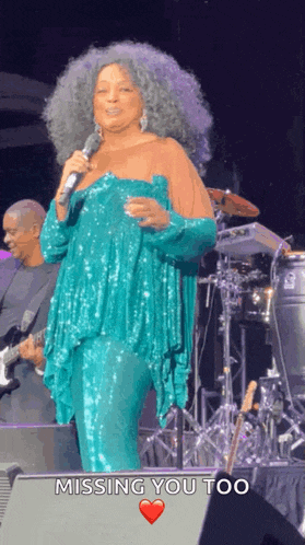 a woman singing into a microphone on a stage with missing you too written on the bottom