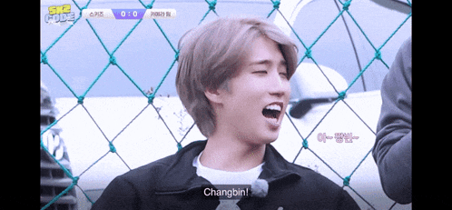 a young man behind a chain link fence with the words changbin on the bottom right
