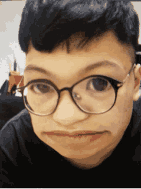 a young man wearing glasses makes a funny face