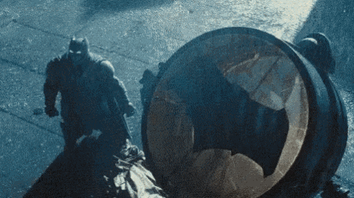 a man in a batman costume is standing next to a barrel with a bat symbol on it .