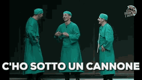 three men in surgical gowns are standing on a stage with the words c ' ho sotto un cannone above them .