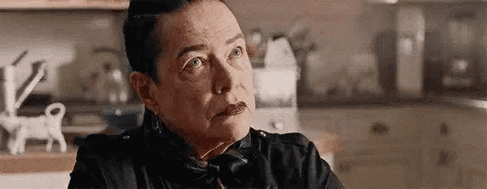 a woman is sitting at a table in a kitchen wearing a black shirt and scarf .