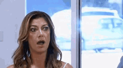 a woman is standing in front of a window with her mouth open and a surprised look on her face .