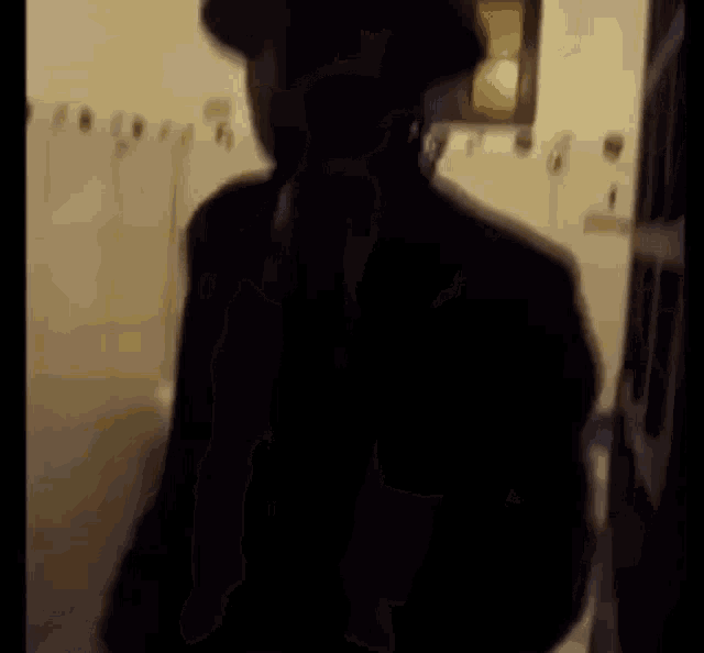 a silhouette of a man in a suit and hat is standing in a bathroom .