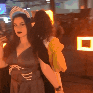 a woman with a crown on her head is standing next to another woman in a dark room