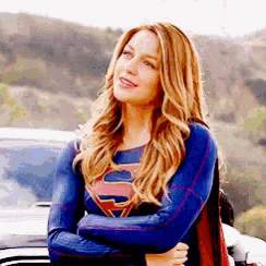 a woman in a superman costume is standing next to a car with her arms crossed .