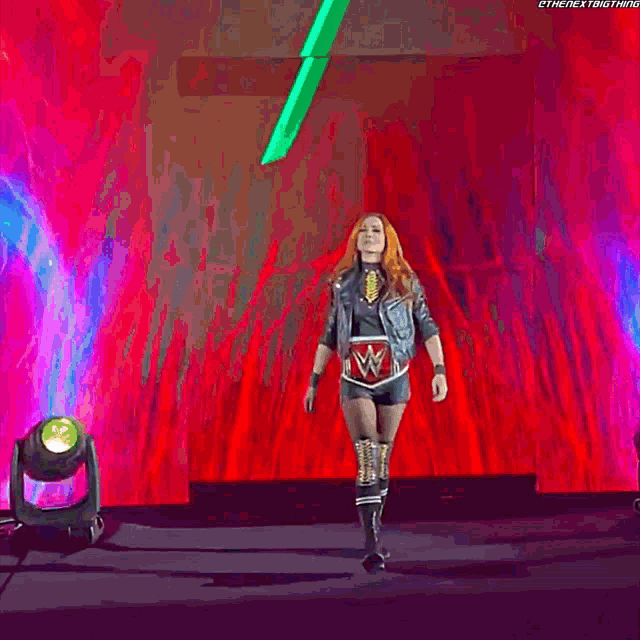 a woman in a wrestling outfit is walking on a stage with a green sword in the background .