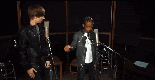 a man in a leather jacket stands next to a boy in a white shirt in front of two microphones