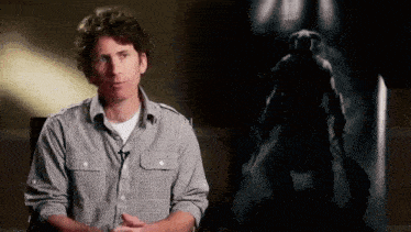 a man in a plaid shirt is sitting in front of a painting of a man holding a sword