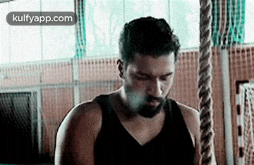 a man in a black tank top is standing next to a rope in a gym .