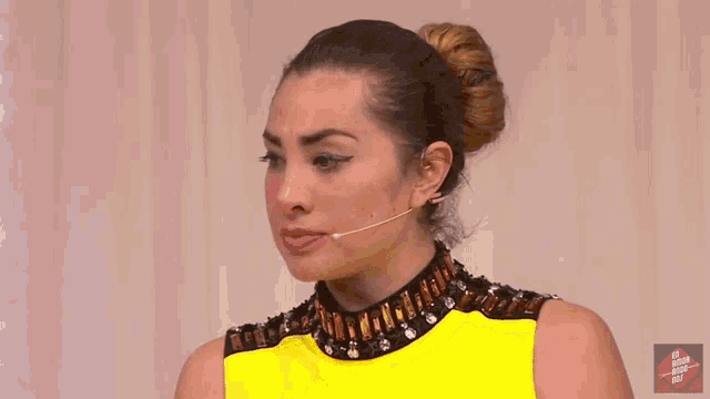 a woman in a yellow dress is talking into a microphone and making a funny face .