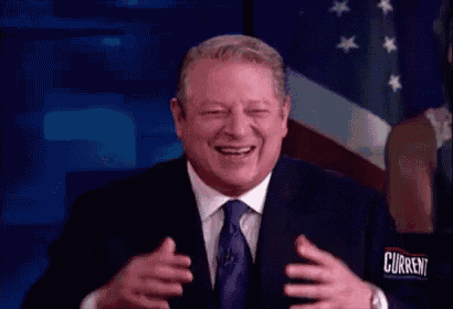 a man in a suit and tie is laughing in front of an american flag with the word current on his shirt