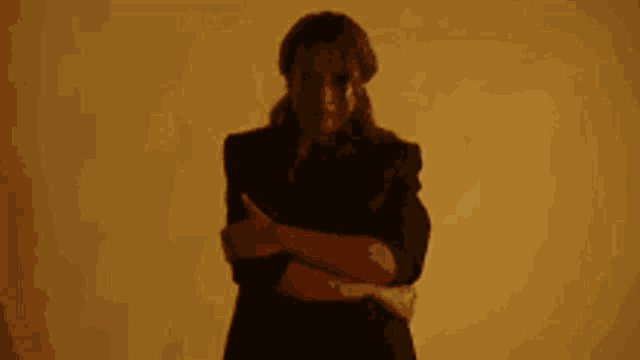 a woman in a black jacket is standing with her arms crossed and looking at the camera .