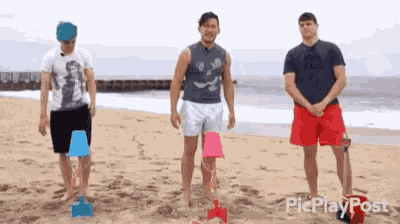 three men are standing on a beach with buckets in their hands .