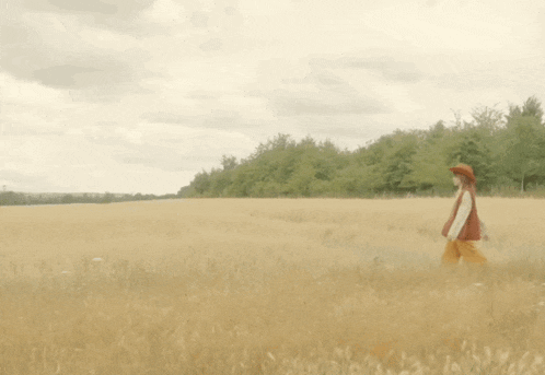 a woman in a hat is walking through a field of tall grass