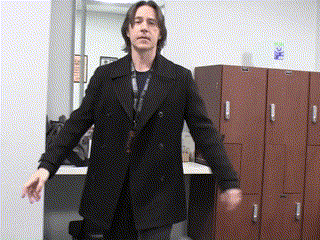 a man in a black coat stands in front of a row of brown lockers