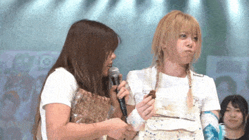 a woman holding a microphone talks to another woman who is holding a piece of wood