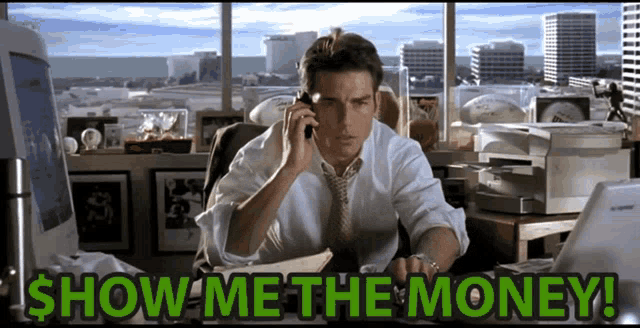 a man is sitting at a desk talking on a cell phone with the words show me the money written below him