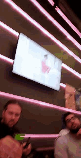 a group of people are sitting in front of a tv with a pink light behind it