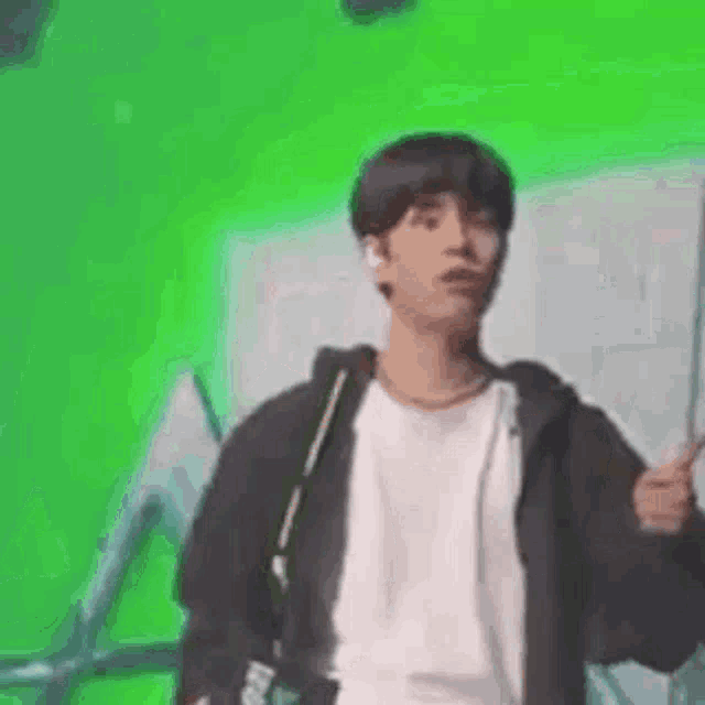 a young man is standing in front of a green screen and holding a camera .
