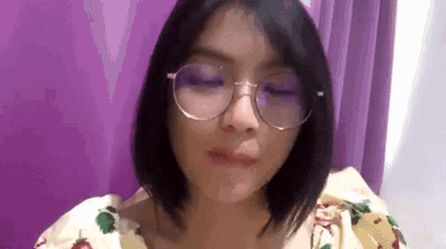 a woman wearing glasses and a floral shirt is making a face .