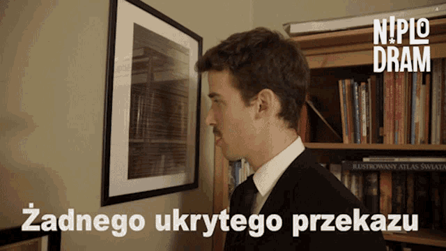 a man in a suit and tie is looking at a picture on a wall with niplo dram written on the bottom right