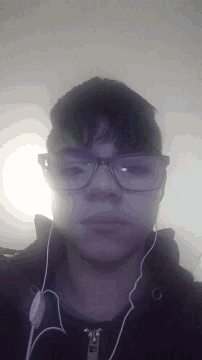 a man wearing glasses and ear buds looks down at the camera