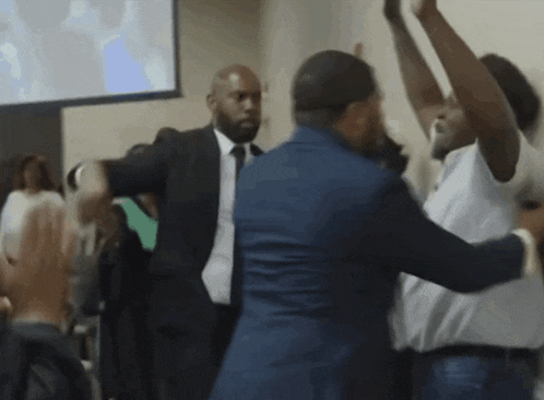a man in a suit and tie is standing in a crowd with his arms in the air