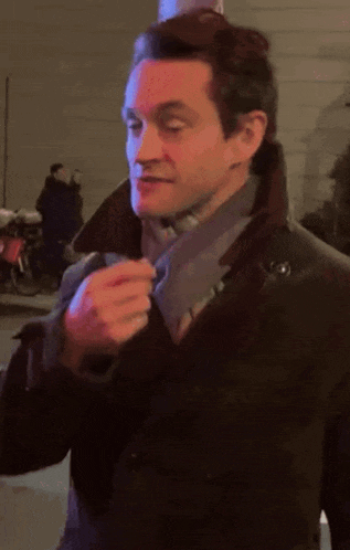 a man wearing a black coat and a scarf is adjusting his tie