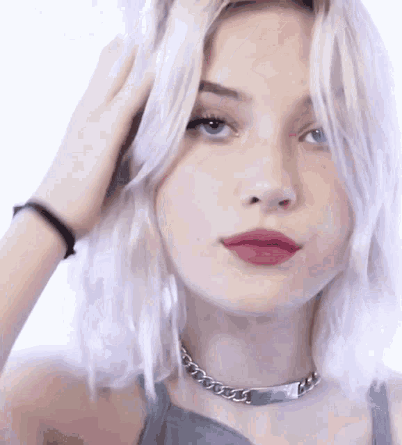 a woman with white hair and red lips is wearing a choker necklace and bracelet .