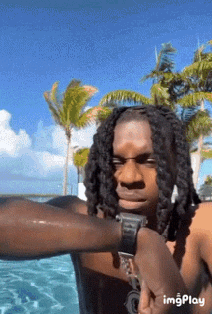 a man with dreadlocks is standing next to a swimming pool .