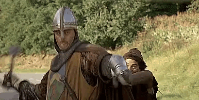 a man in a knight 's armor is standing next to a woman in a field holding a sword .