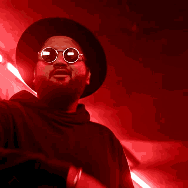a man wearing a black hat and round sunglasses in a red room