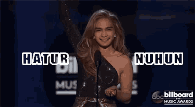 a woman stands on a stage with her arms in the air and the words hatur nuhun above her
