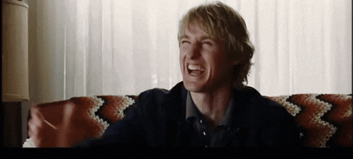 a man is sitting on a couch and laughing with his mouth open