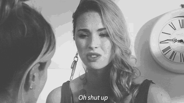a woman is talking to another woman in front of a clock and says " oh shut up "