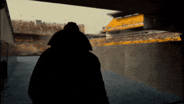 a man in a black coat is walking through a tunnel towards a stadium