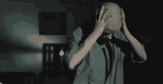 a man in a green shirt is holding his head in his hands in a dark room .