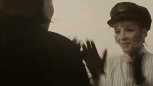 a woman in a hat and gloves is shaking hands with a man in a suit .