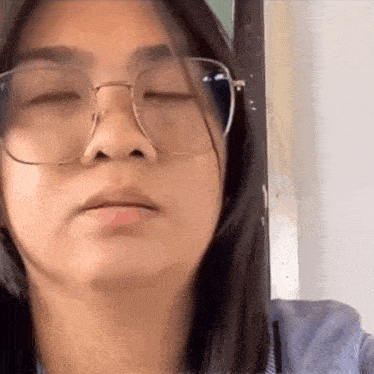 a woman wearing glasses and a blue shirt is making a funny face .