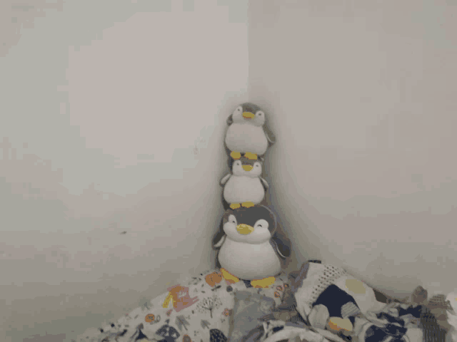 four stuffed penguins stacked on top of each other in a corner