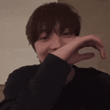 a man covering his mouth with his hand while wearing a black shirt