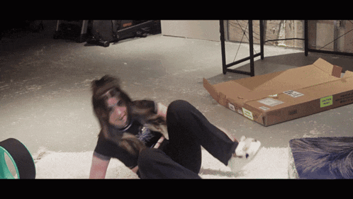 a person laying on the floor next to a cardboard box with a green sticker on it that says " fragile "