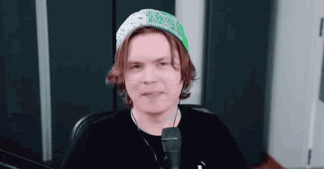 a man wearing a green hat and a black shirt is sitting in front of a microphone .