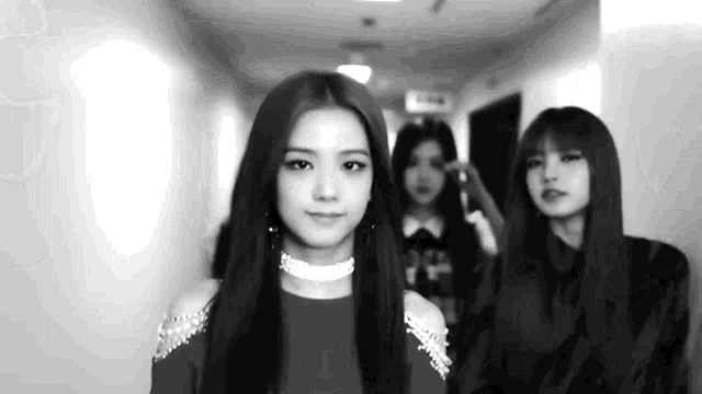 a black and white photo of a woman standing in a hallway with two other women .