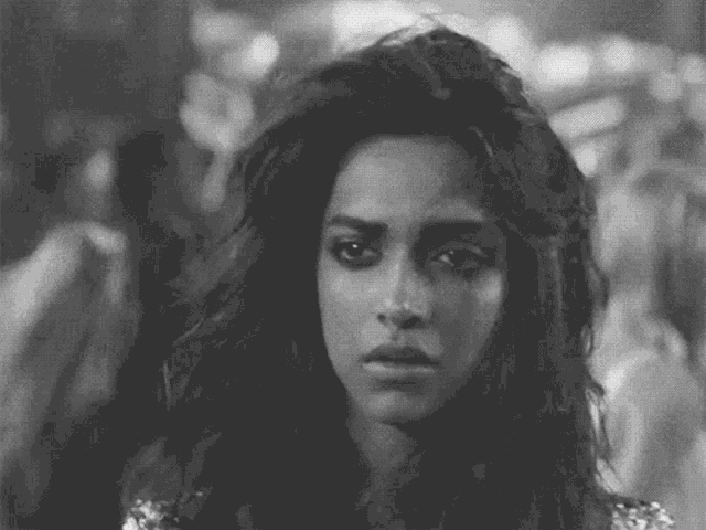 a black and white photo of a woman with long hair looking at the camera with a serious look on her face .
