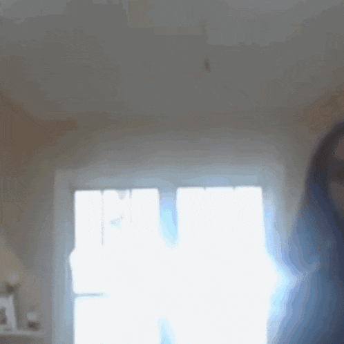 a woman is standing in front of a window and a lamp